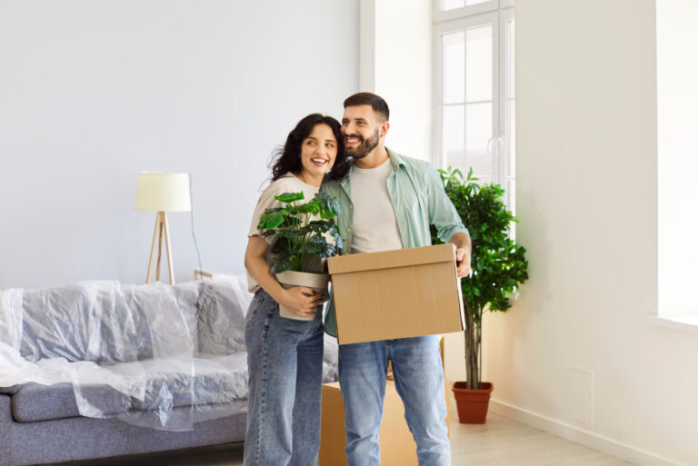 Young couple carrying moving boxes and a houseplant into a new rental home, representing tenants moving to Portslade or Fishersgate.