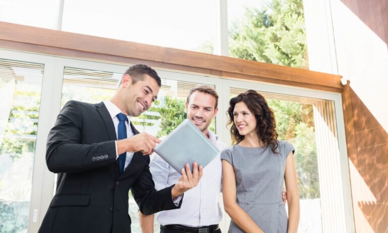Estate agent showing property information on a tablet to a couple inside a modern home, illustrating a property valuation and sales consultation for homeowners selling in Wolverhampton in 2026.