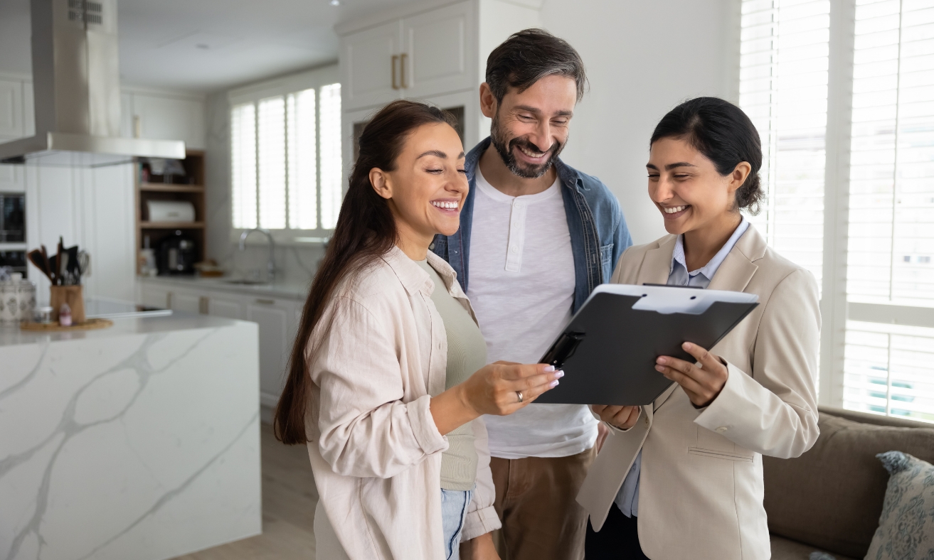A first-time buyer couple reviews property details with an estate agent inside a modern home, illustrating the home-buying process discussed in the Swansea first-time buyer guide for 2026.